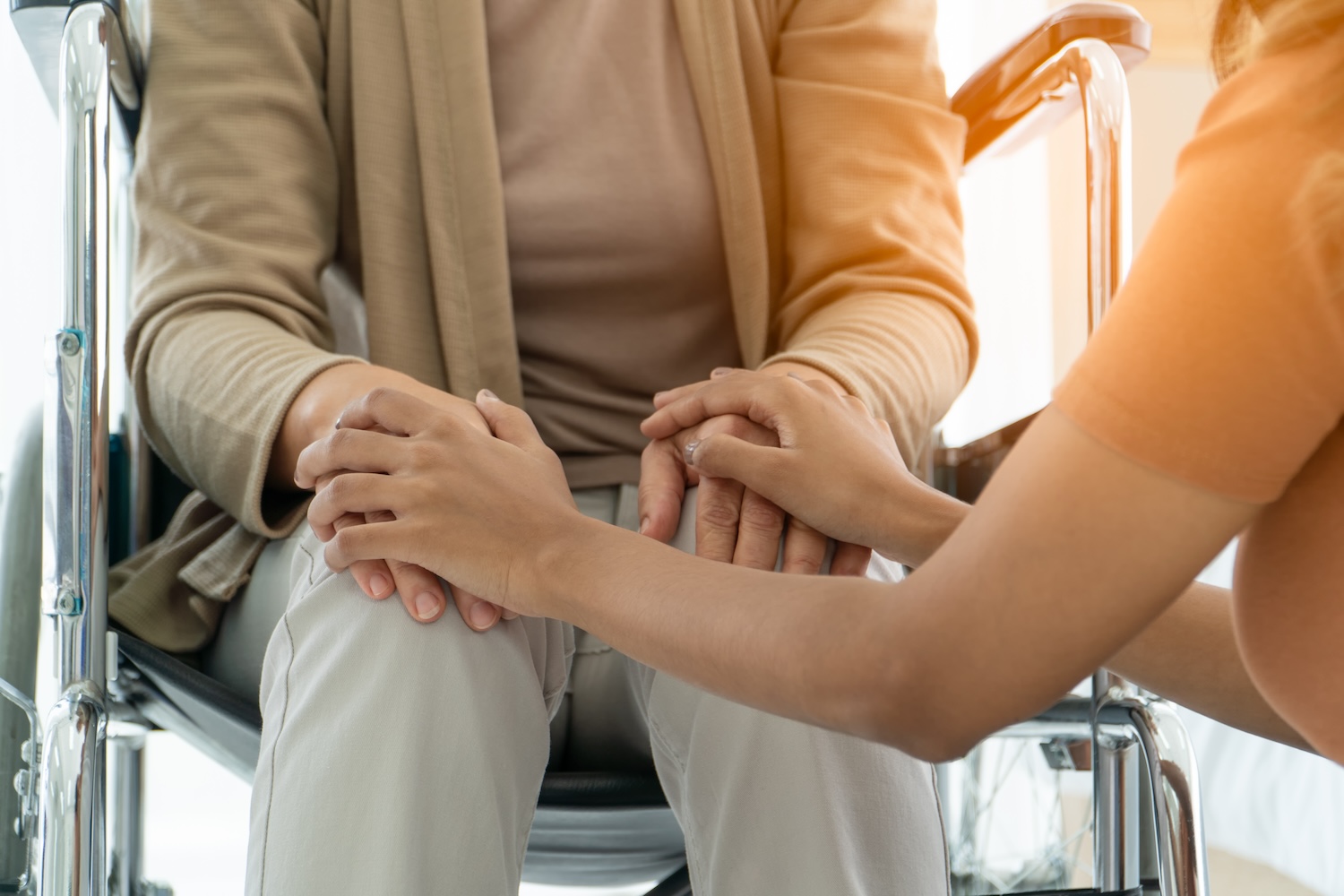 Older woman in wheelchair holding hands with another women