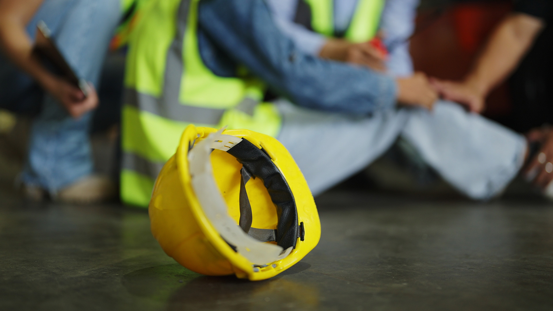Construction worker holding knee injury with hardhat next to him