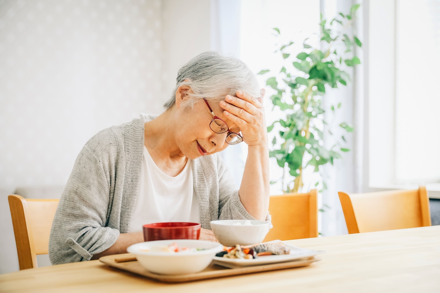 Elderly asian women holding head with meal infront of her