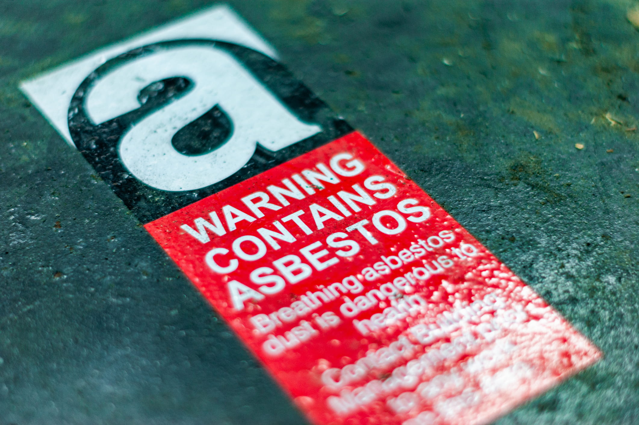 Close-up of a red and white warning label indicating the material contains asbestos and poses a health hazard.