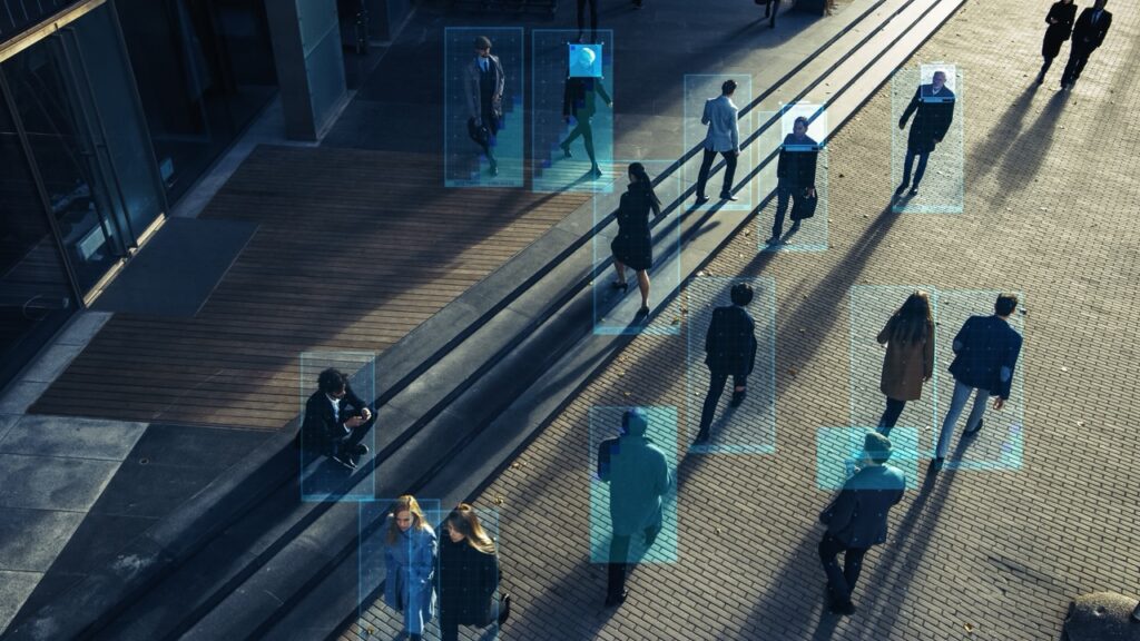 People walking through an urban plaza with digital facial recognition overlays identifying individuals using AI technology for digital evidence.
